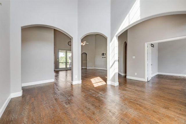 spare room featuring a high ceiling, baseboards, dark wood finished floors, and a ceiling fan