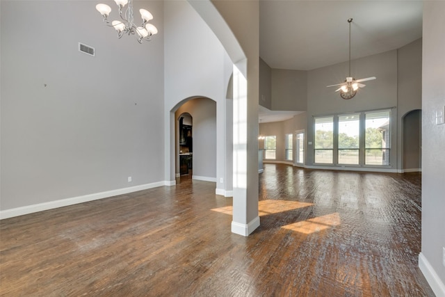 unfurnished living room featuring arched walkways, a high ceiling, dark wood-style flooring, visible vents, and baseboards