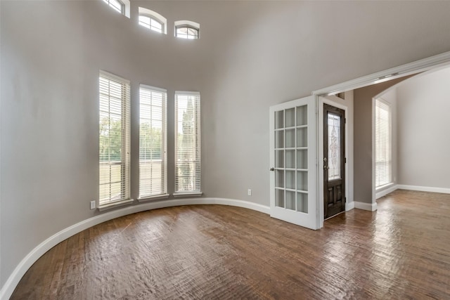 empty room featuring arched walkways, a high ceiling, and baseboards