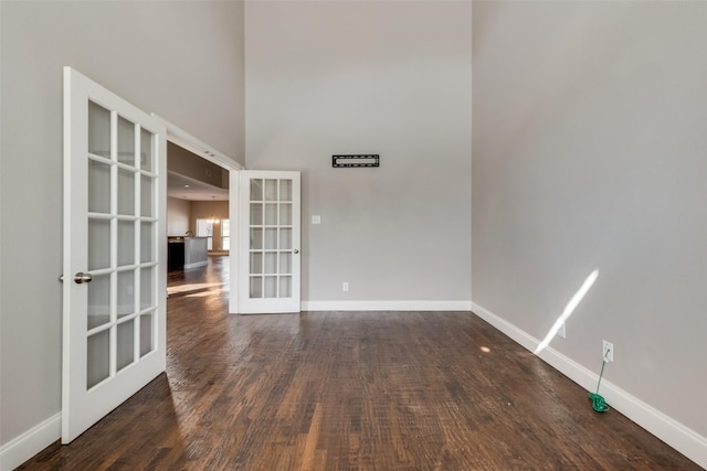 unfurnished room featuring a towering ceiling, baseboards, dark wood-style flooring, and french doors