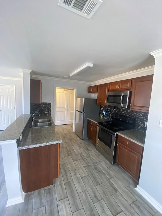 kitchen featuring visible vents, appliances with stainless steel finishes, a peninsula, a sink, and backsplash