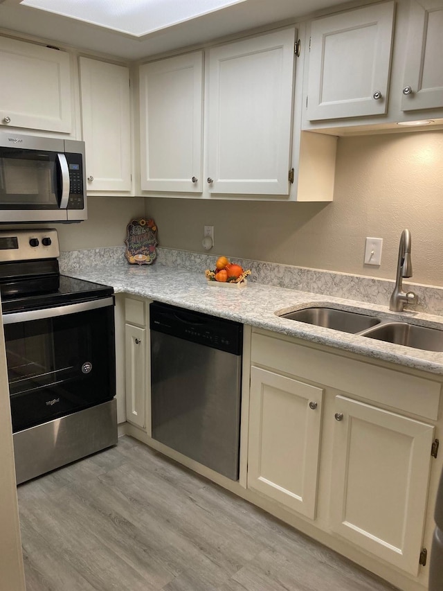 kitchen with light wood finished floors, stainless steel appliances, a sink, and light countertops