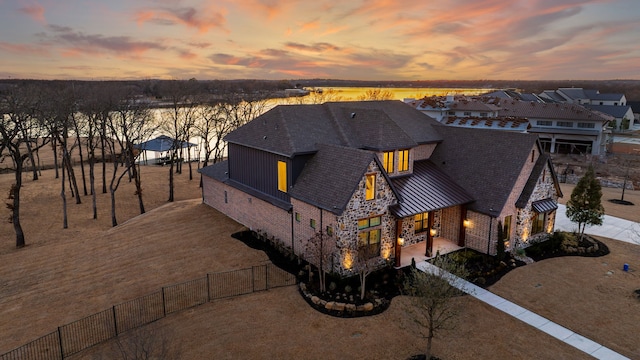 view of front of property featuring stone siding, a residential view, fence, and a standing seam roof