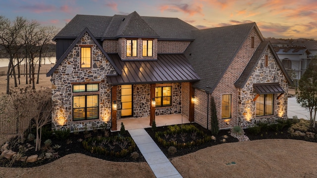 view of front of home with a patio, a shingled roof, a standing seam roof, metal roof, and stone siding