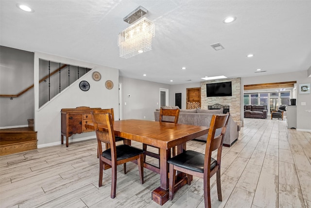 dining room with light wood-type flooring, visible vents, a fireplace, and stairway