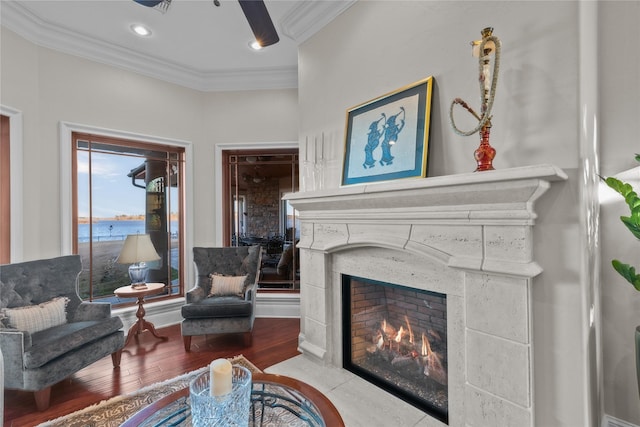 living area with recessed lighting, a water view, wood finished floors, a fireplace with flush hearth, and crown molding