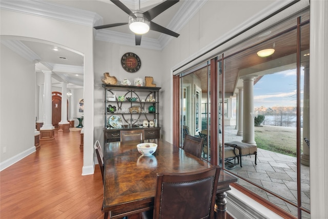 dining space with arched walkways, wood finished floors, a ceiling fan, ornamental molding, and ornate columns