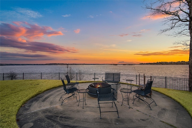 patio terrace at dusk featuring a yard, a water view, fence, and a fire pit