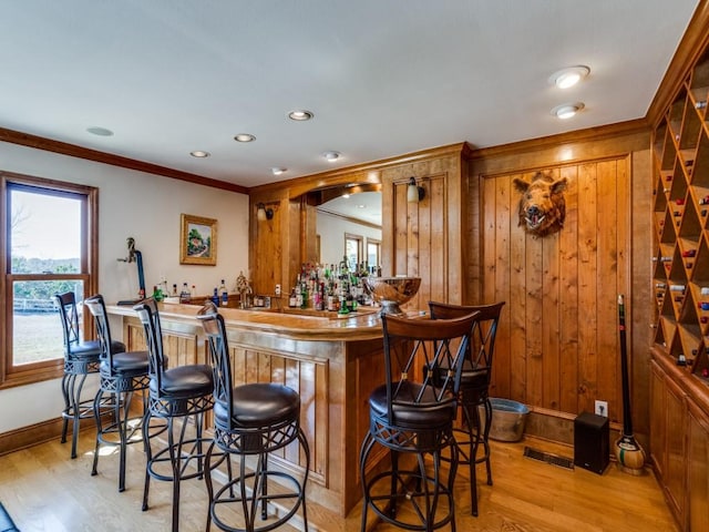 bar with visible vents, ornamental molding, light wood-style floors, indoor wet bar, and baseboards