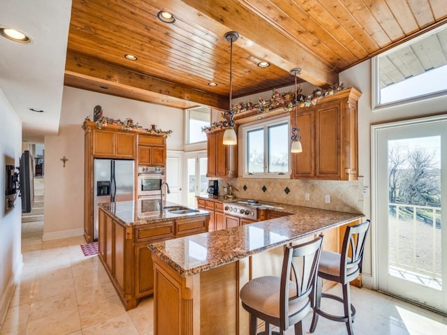 kitchen featuring dark stone countertops, an island with sink, a sink, brown cabinets, and backsplash