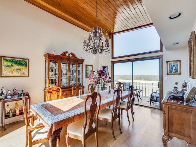 dining area featuring an inviting chandelier, light wood-style flooring, a towering ceiling, and wooden ceiling