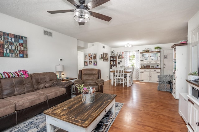 living area featuring a ceiling fan, a textured ceiling, visible vents, and wood finished floors