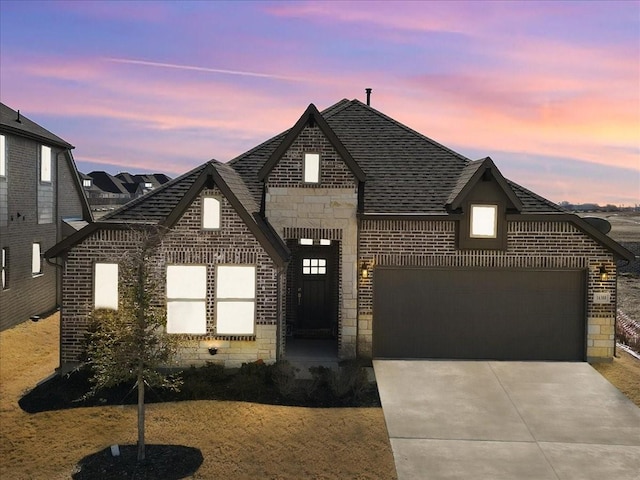 french country style house featuring a garage, stone siding, brick siding, and driveway