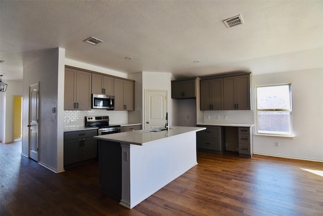 kitchen featuring light countertops, visible vents, appliances with stainless steel finishes, a sink, and an island with sink