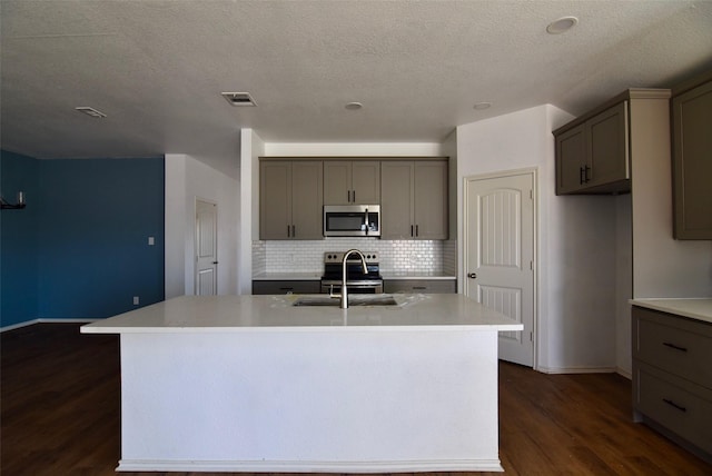 kitchen with stainless steel appliances, light countertops, a sink, and a center island with sink