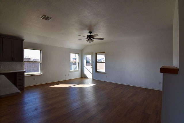 empty room featuring a wealth of natural light, dark wood-style flooring, visible vents, and a ceiling fan