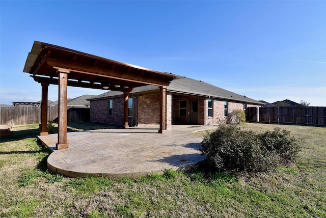 rear view of property featuring a yard, a patio, brick siding, and a fenced backyard