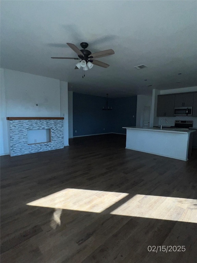 unfurnished living room with visible vents, dark wood finished floors, a ceiling fan, a fireplace, and a sink