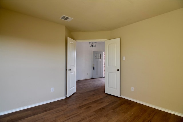 spare room with dark wood-style flooring, visible vents, and baseboards