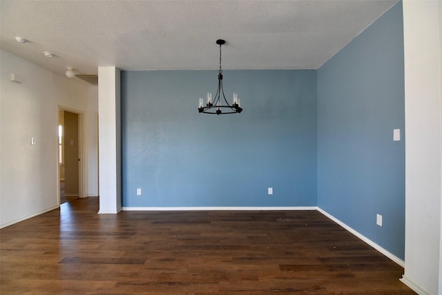 spare room featuring dark wood-style floors, baseboards, a textured ceiling, and an inviting chandelier