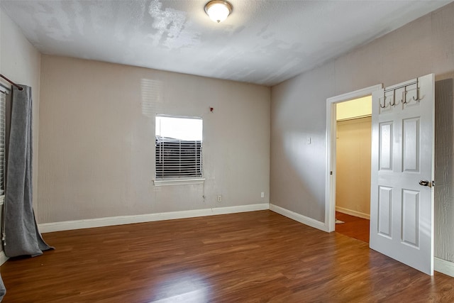 empty room with a textured ceiling, baseboards, and dark wood-type flooring