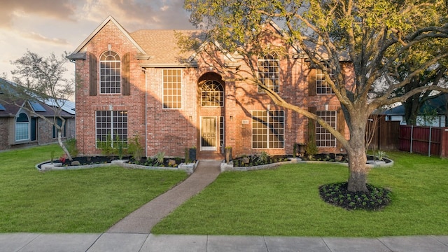 traditional home with brick siding, a front yard, and fence