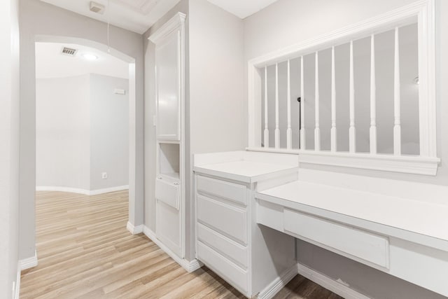 corridor featuring visible vents, baseboards, arched walkways, and light wood-style flooring