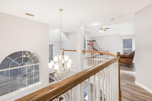 hall with wood finished floors, an upstairs landing, visible vents, and baseboards