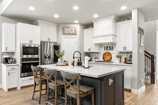 kitchen featuring stainless steel appliances, white cabinetry, a kitchen breakfast bar, light countertops, and an island with sink