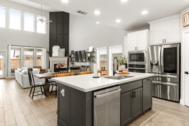 kitchen featuring a kitchen island with sink, white cabinets, open floor plan, light countertops, and appliances with stainless steel finishes