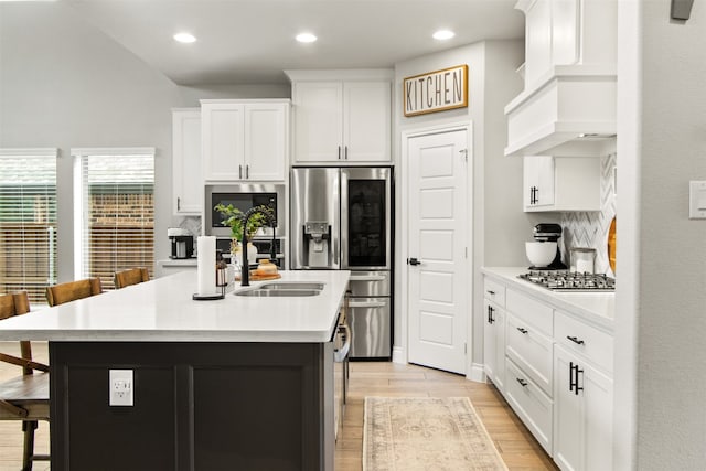 kitchen with a kitchen island with sink, light countertops, a kitchen bar, and white cabinetry