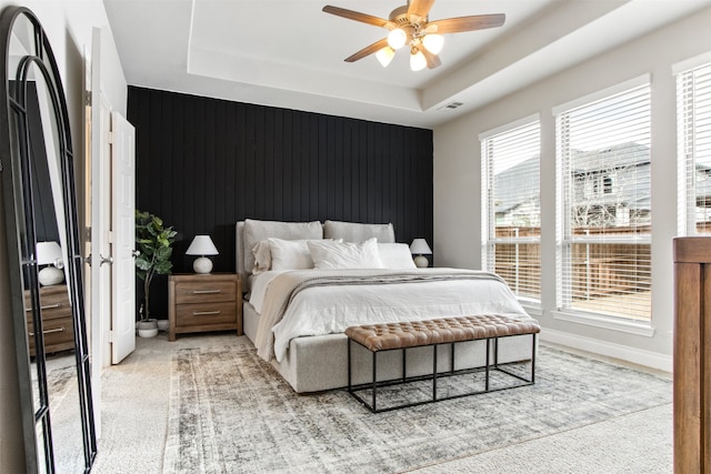 bedroom with a tray ceiling, light colored carpet, visible vents, and baseboards