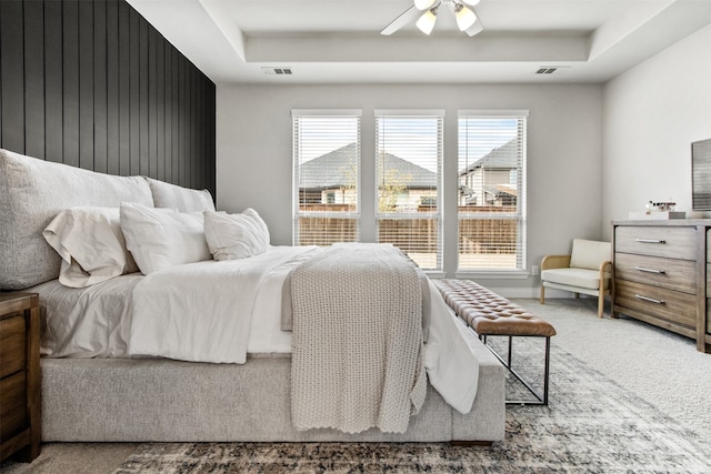 carpeted bedroom featuring ceiling fan, a tray ceiling, and visible vents