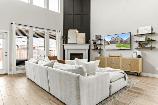 living room featuring a towering ceiling, a brick fireplace, light wood-style flooring, and baseboards