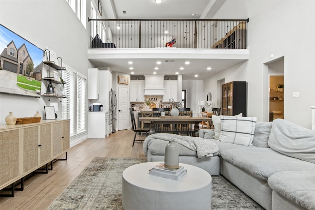 living area featuring light wood-type flooring, a towering ceiling, and recessed lighting