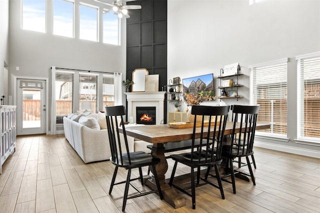 dining room featuring ceiling fan, light wood finished floors, plenty of natural light, and a glass covered fireplace