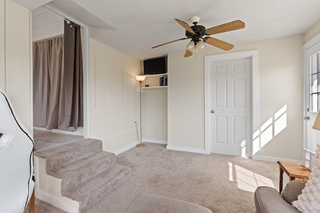 carpeted living area with a ceiling fan, baseboards, and stairs