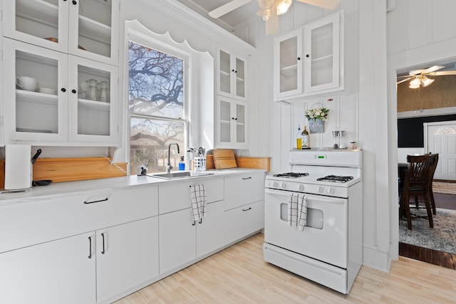 kitchen with light countertops, light wood-style flooring, a ceiling fan, white range with gas cooktop, and a sink