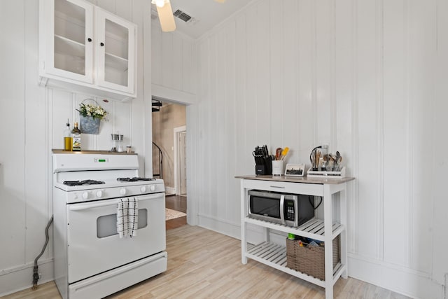 kitchen featuring light wood finished floors, white range with gas stovetop, stainless steel microwave, and white cabinets