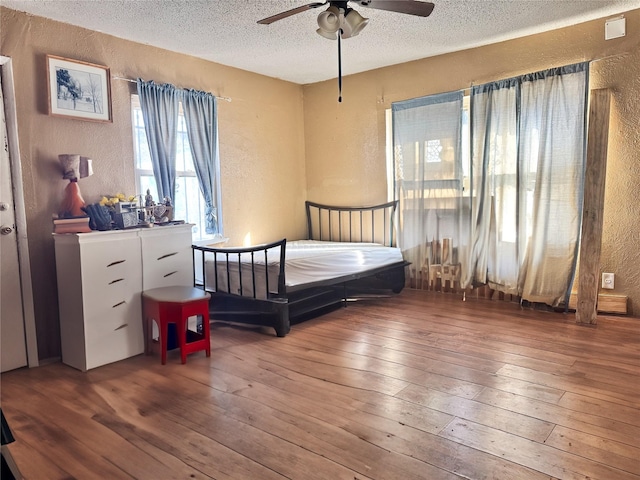 bedroom with ceiling fan, a textured wall, a textured ceiling, and wood finished floors