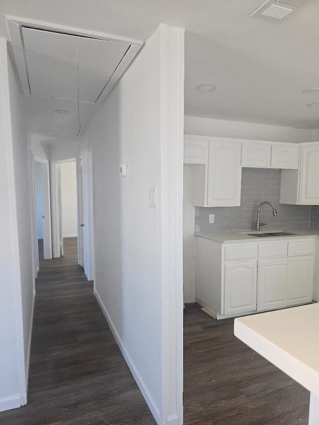 corridor with dark wood-style flooring, visible vents, attic access, a sink, and baseboards