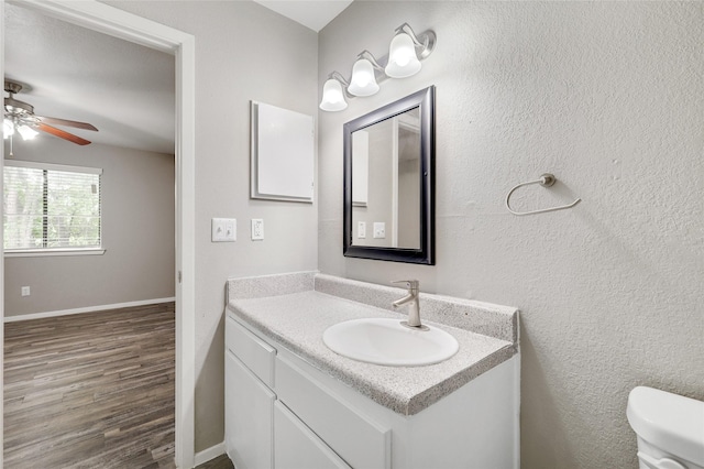 half bath featuring toilet, wood finished floors, vanity, baseboards, and a ceiling fan