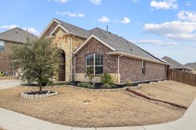 view of property exterior featuring stone siding, a shingled roof, fence, and brick siding