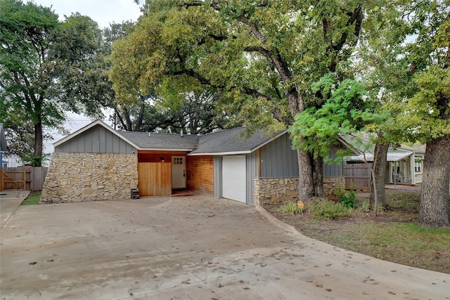 view of front of property with a garage, stone siding, board and batten siding, and fence