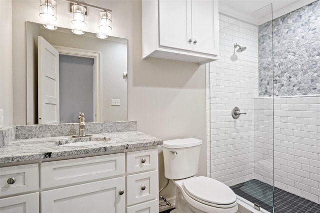 bathroom with a tile shower, vanity, and toilet