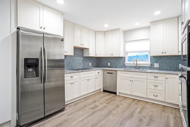 kitchen featuring stainless steel appliances, light wood-style flooring, white cabinets, a sink, and light stone countertops