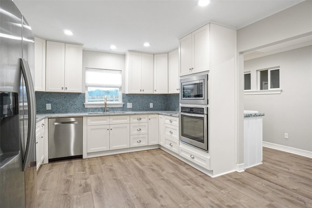 kitchen featuring appliances with stainless steel finishes, light wood-style flooring, a sink, and white cabinetry