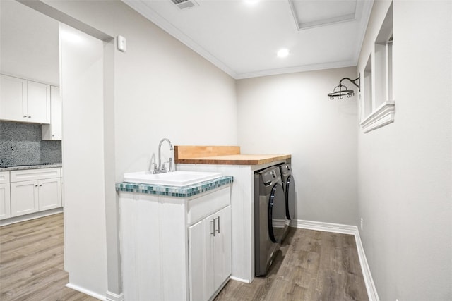 washroom featuring washer and clothes dryer, ornamental molding, a sink, light wood-type flooring, and baseboards