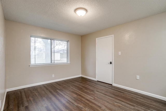 empty room with dark wood-style floors, a textured ceiling, and baseboards