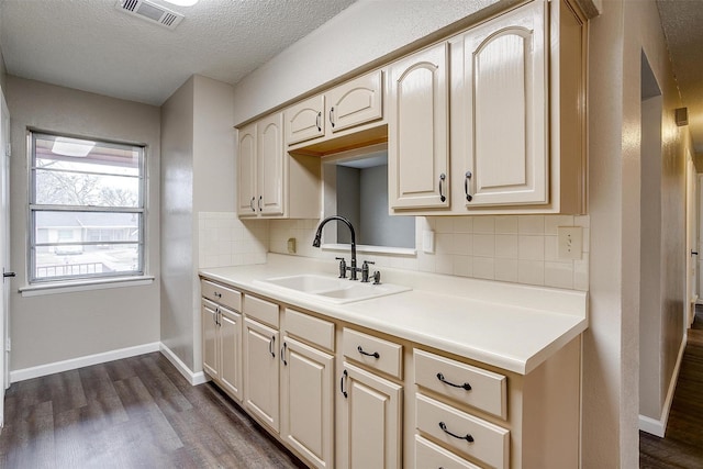 kitchen featuring dark wood-style flooring, a sink, visible vents, light countertops, and backsplash